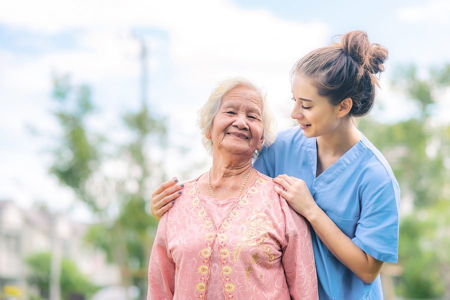 A smiling senior woman outdoors with her caregiver